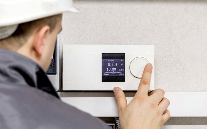 Un técnico de climatización, con casco de seguridad, ajusta un termostato digital programable en la pared.