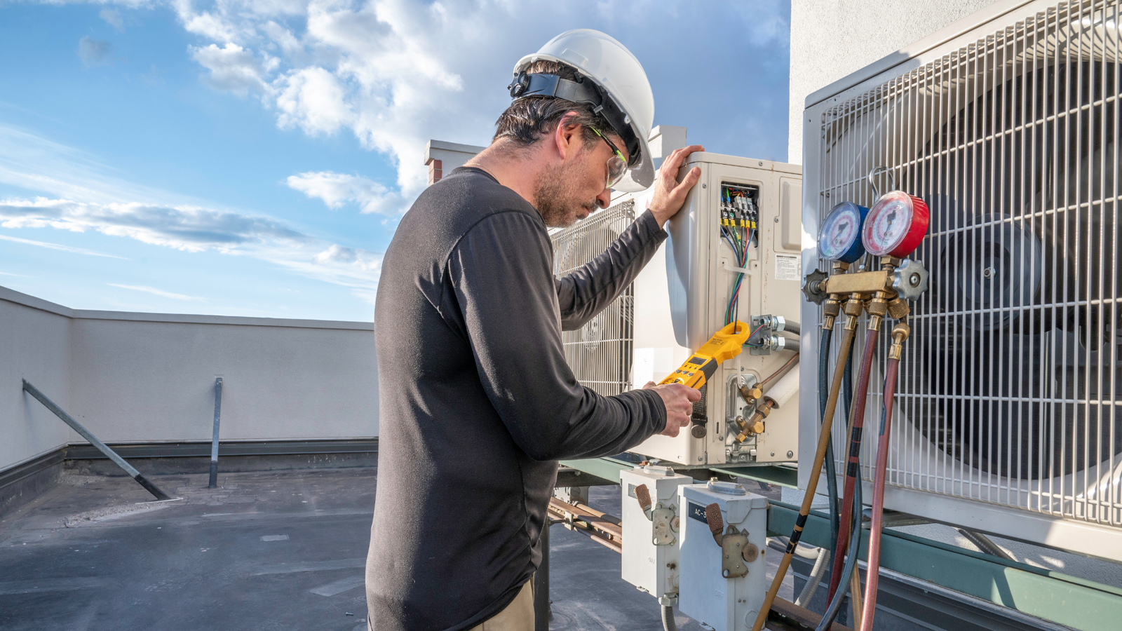 Técnico haciendo revisión a una unodad externa de aire acondicionado con un manómetro al lado