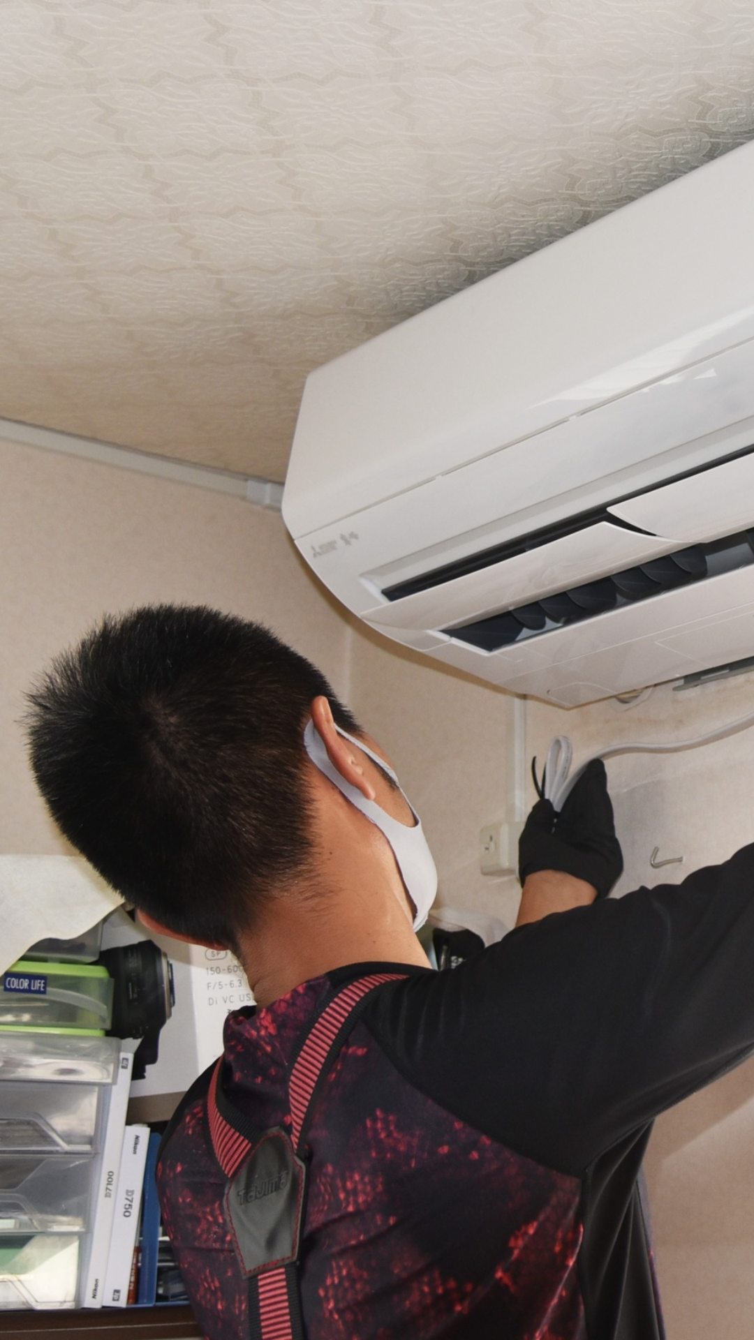 Técnico profesional con mascarilla instalando una unidad de aire acondicionado Mitsubishi montada en la pared.